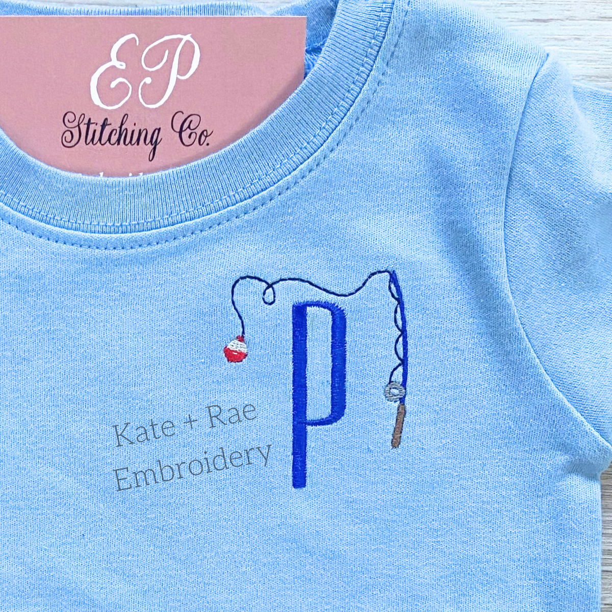 Fishing Pole Mini Fill Embroidery Design: Small fishing pole with a red and white bobber beside a blue letter P on a light blue shirt