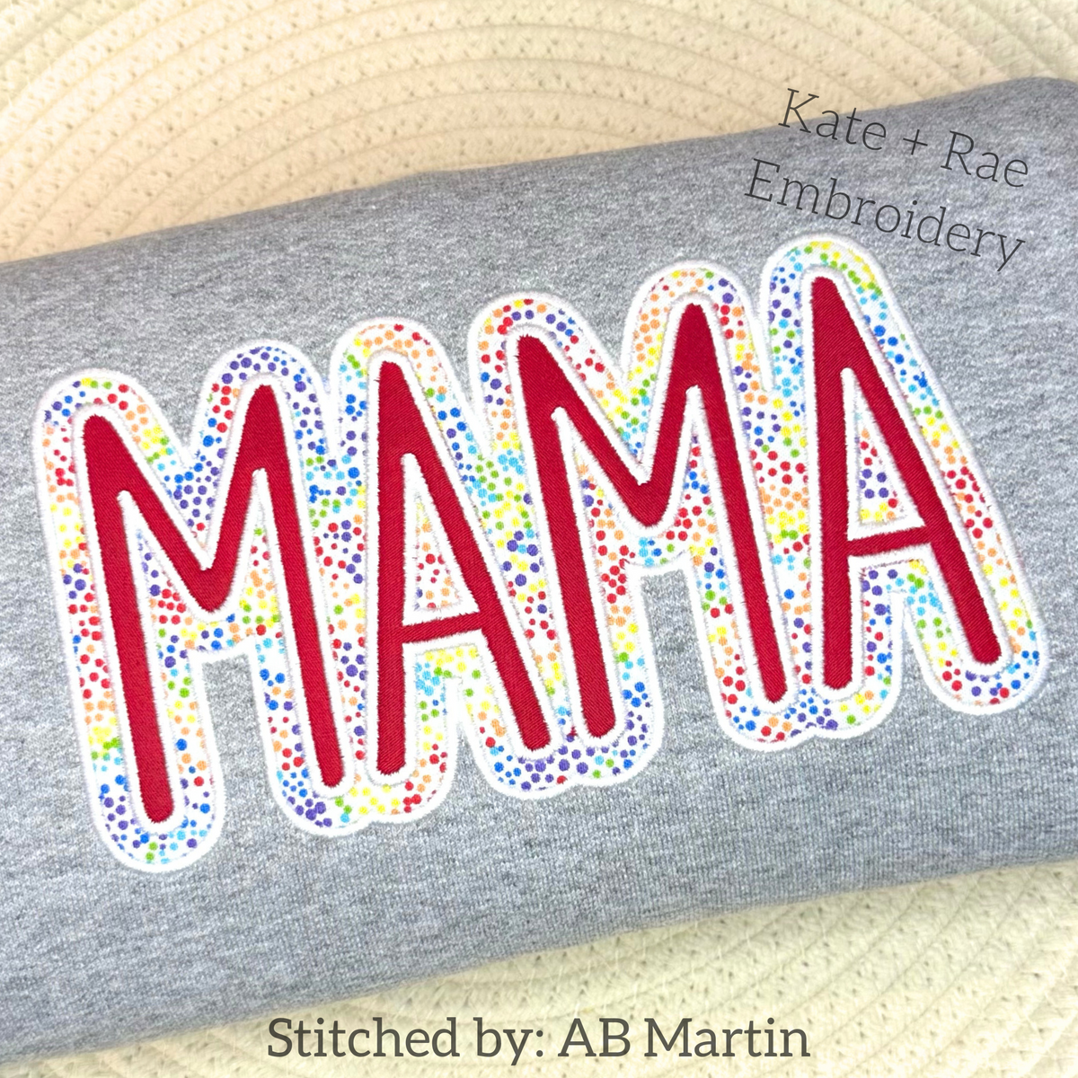 MAMA Double Satin Stitch Applique Embroidery Design: The word MAMA in red letters with a rainbow speckled double outline on a gray sweatshirt