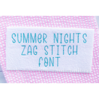 Summer Nights Zag Stitch Embroidery Font: The words Summer Nights Zag Stitch Font stitched in teal on white fabric over pink seersucker