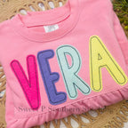 Simple Life Bean Stitch Applique Embroidery Font: The name Vera in hot pink, purple, mint, and yellow applique letters on a pink sweatshirt
