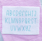 Summer Nights Zag Stitch Embroidery Font: Uppercase A to Z alphabet stitched in teal on white fabric over pink seersucker