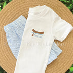 Canoe Mini Fill Embroidery Design: Small canoe and the name Lincoln stitched on the chest of a white shirt with blue seersucker shorts